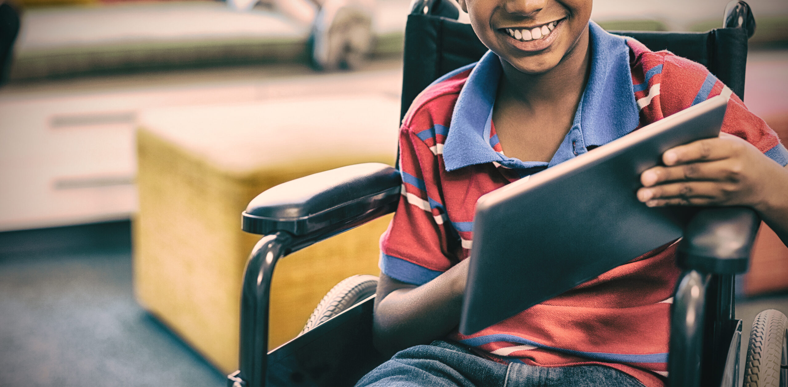 Portrait of disabled schoolboy on wheelchair using digital tablet in library at school
